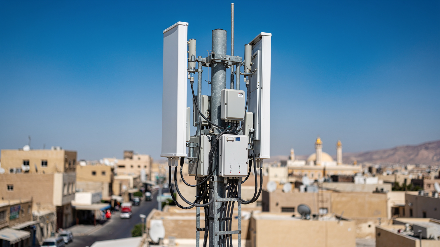 Sebuah menara BTS seluler modern dengan latar belakang langit biru cerah di Makkah, menunjukkan infrastruktur telekomunikasi yang kuat di Arab Saudi.