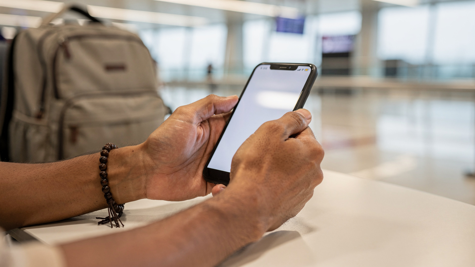 Tangan seorang jamaah haji memegang ponsel pintar dan memindai kode QR eSIM di bandara Jeddah, dengan tas travel di sampingnya, menandakan persiapan konektivitas.