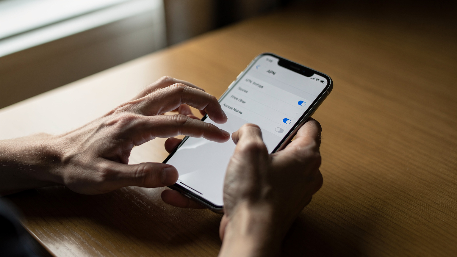 Nærbilde av en reisende sine hender som navigerer gjennom innstillingsmenyen på en smarttelefon, med fokus på valget av APN-innstillinger.