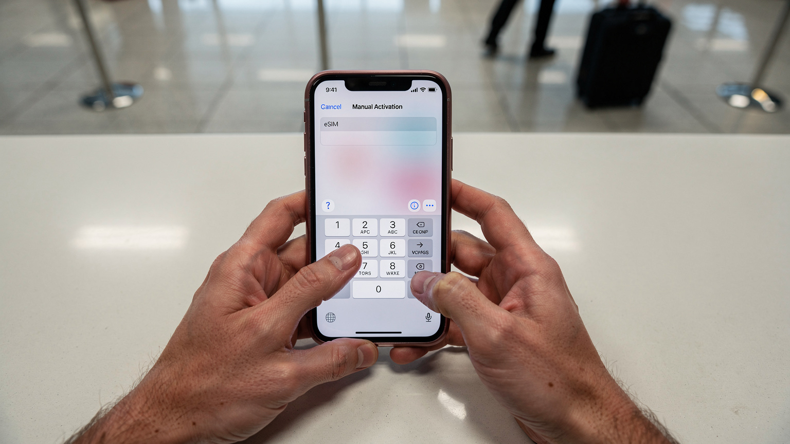 Un primer plano de las manos de un viajero introduciendo manualmente los detalles de activación de una eSIM en un iPhone, con un fondo ligeramente desenfocado de un mostrador de facturación de aeropuerto.