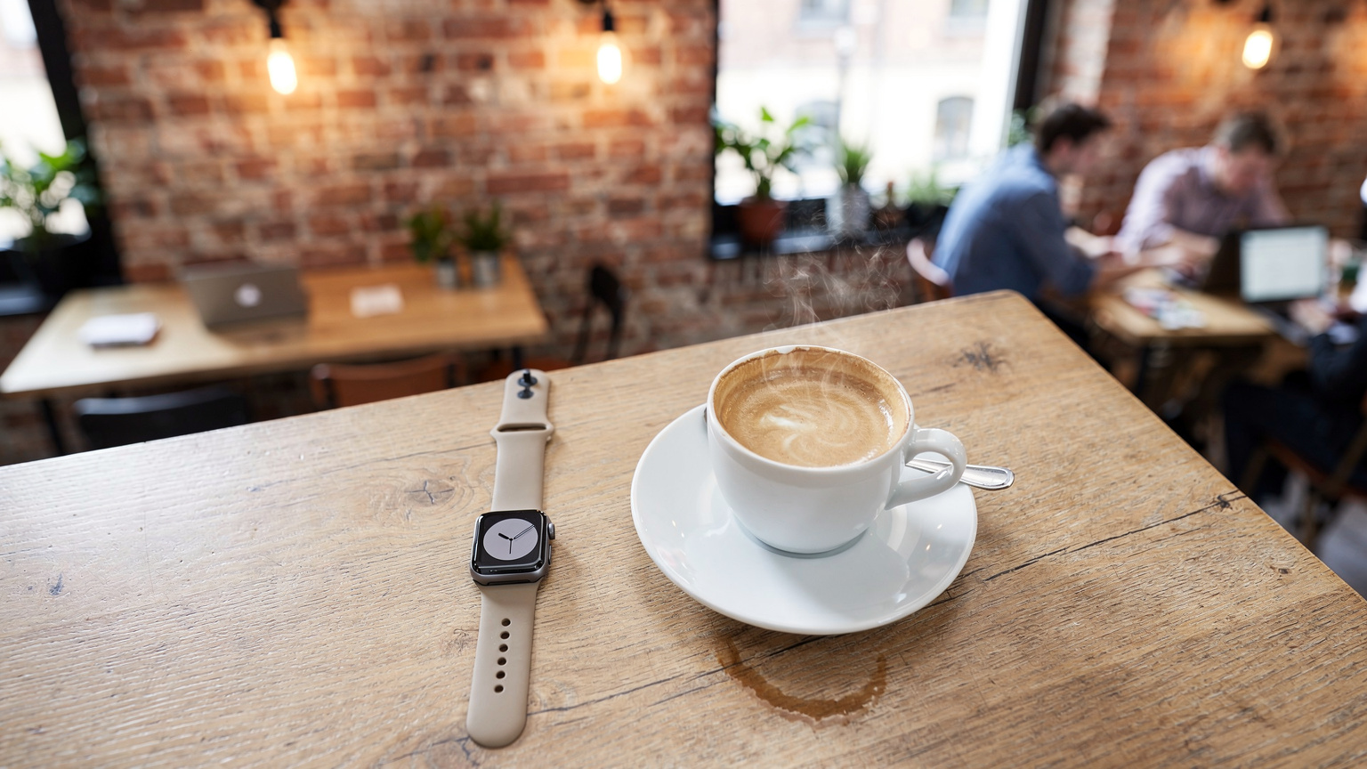 Un café animé dans le quartier de Prenzlauer Berg à Berlin, avec des personnes travaillant sur des ordinateurs portables, et une Apple Watch posée à côté d'une tasse de café sur une table en bois.