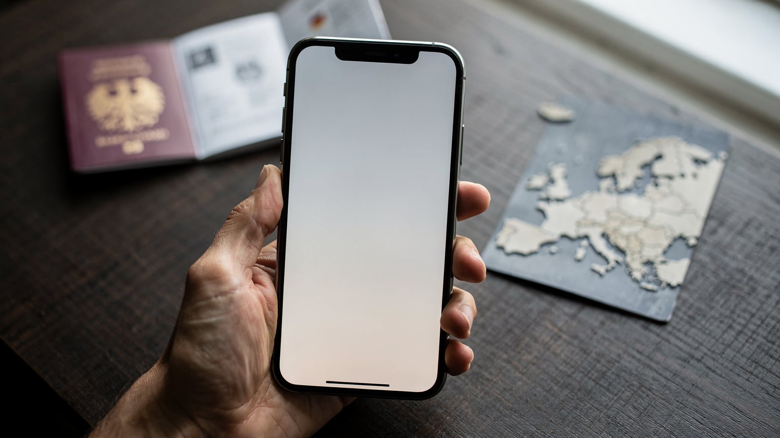 Nahaufnahme einer Hand, die ein Smartphone hält, wobei der Bildschirm eine eSIM-Installationsanleitung oder ein Länderauswahlmenü anzeigt, im Hintergrund ein Reisepass.