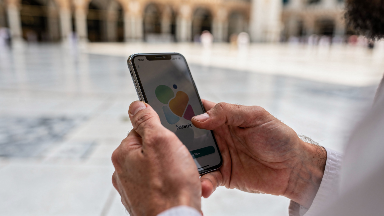 Gros plan sur les mains d'un pèlerin francophone utilisant l'application Nusuk sur son smartphone, montrant l'importance de la connectivité pour la gestion des rituels du Hajj.