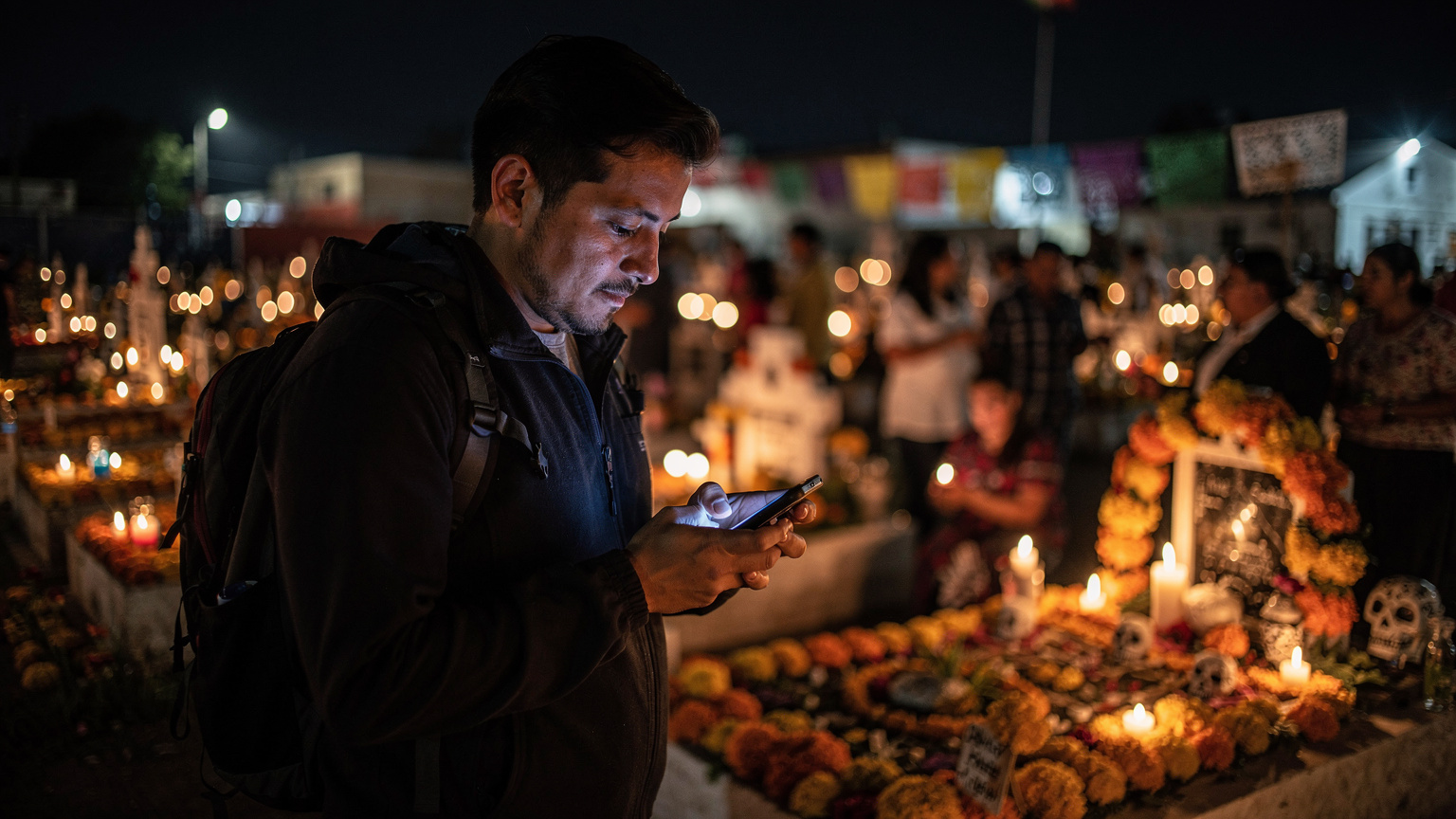 Un viajero hispanohablante, inmerso en la atmósfera del Panteón de San Andrés Mixquic, consulta discretamente su teléfono inteligente, rodeado de ofrendas y velas durante la noche del Día de Muertos.