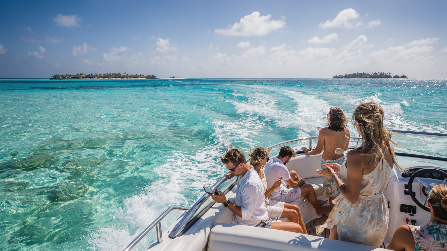 A speed boat cuts through turquoise waters in the Maldives, with passengers enjoying the view and one person subtly checking their phone, highlighting connectivity during transfers.