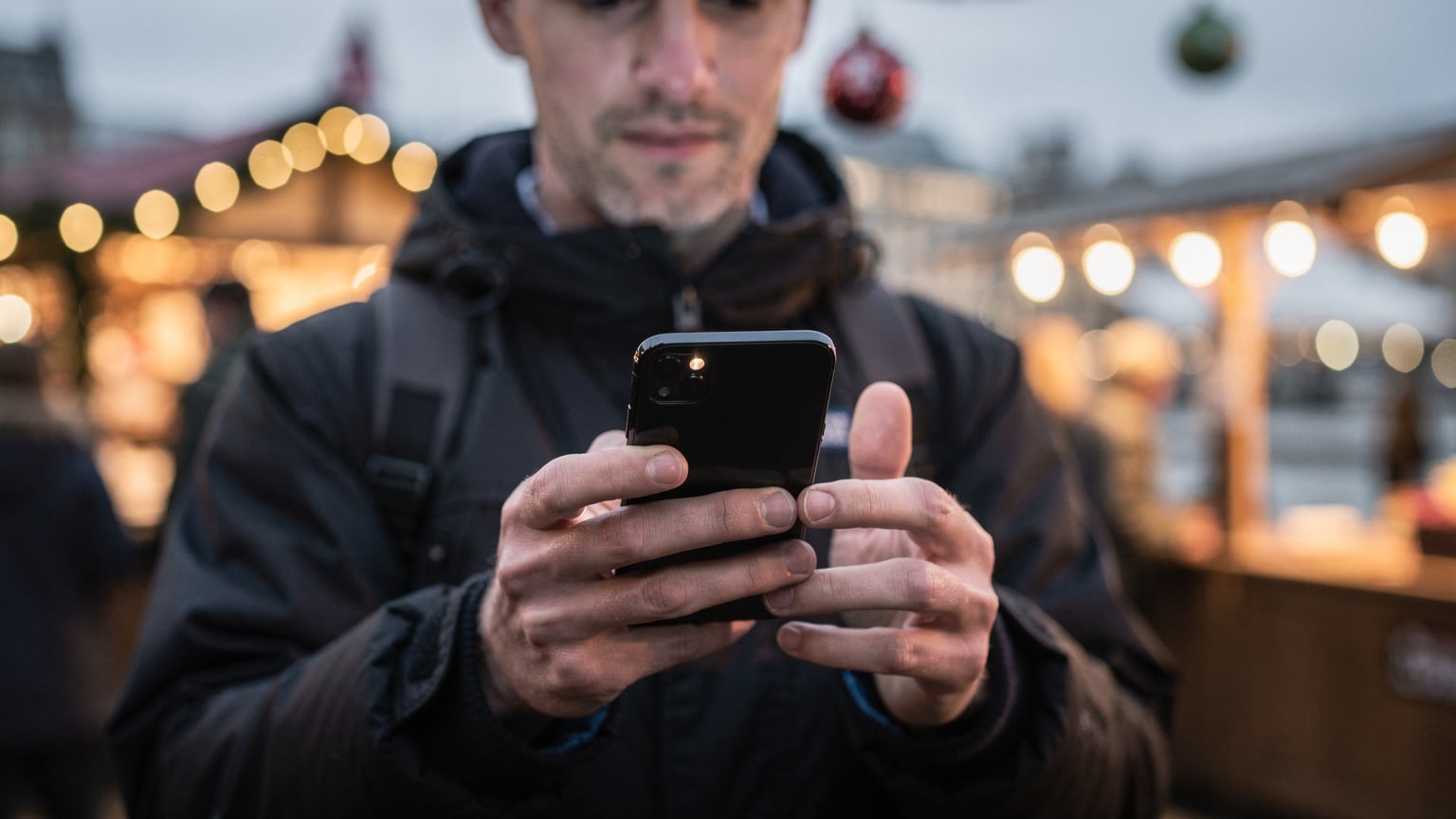 A traveler effortlessly activates their eSIM on a smartphone, displaying the convenience of digital connectivity while surrounded by the bustling, festive atmosphere of a London Christmas market, making it easy to share holiday moments.