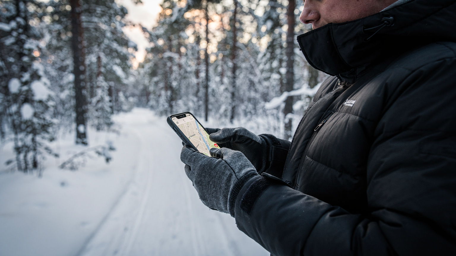A traveler uses a mapping app on their phone to navigate snowy trails in Nordmarka, Oslo, with a dense forest visible in the background.