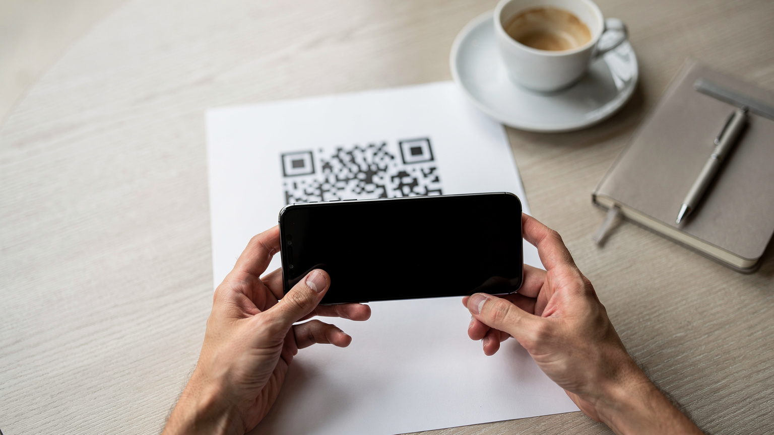A person's hands holding a smartphone and scanning a QR code from a printed paper, set against a bright, clean cafe table, illustrating the simple digital eSIM activation process.