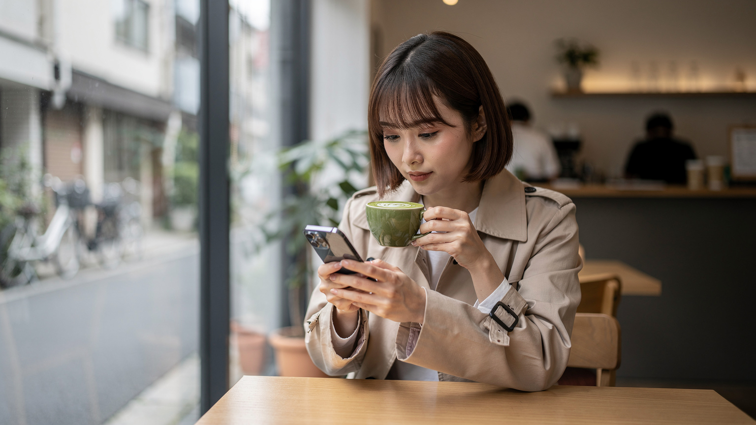 Japonya'da, modern ve minimalist bir kafenin penceresinden içeri süzülen yumuşak sabah ışığında, bir gezginin iPhone 17'sinden eSIM ayarlarını kontrol ettiği an.