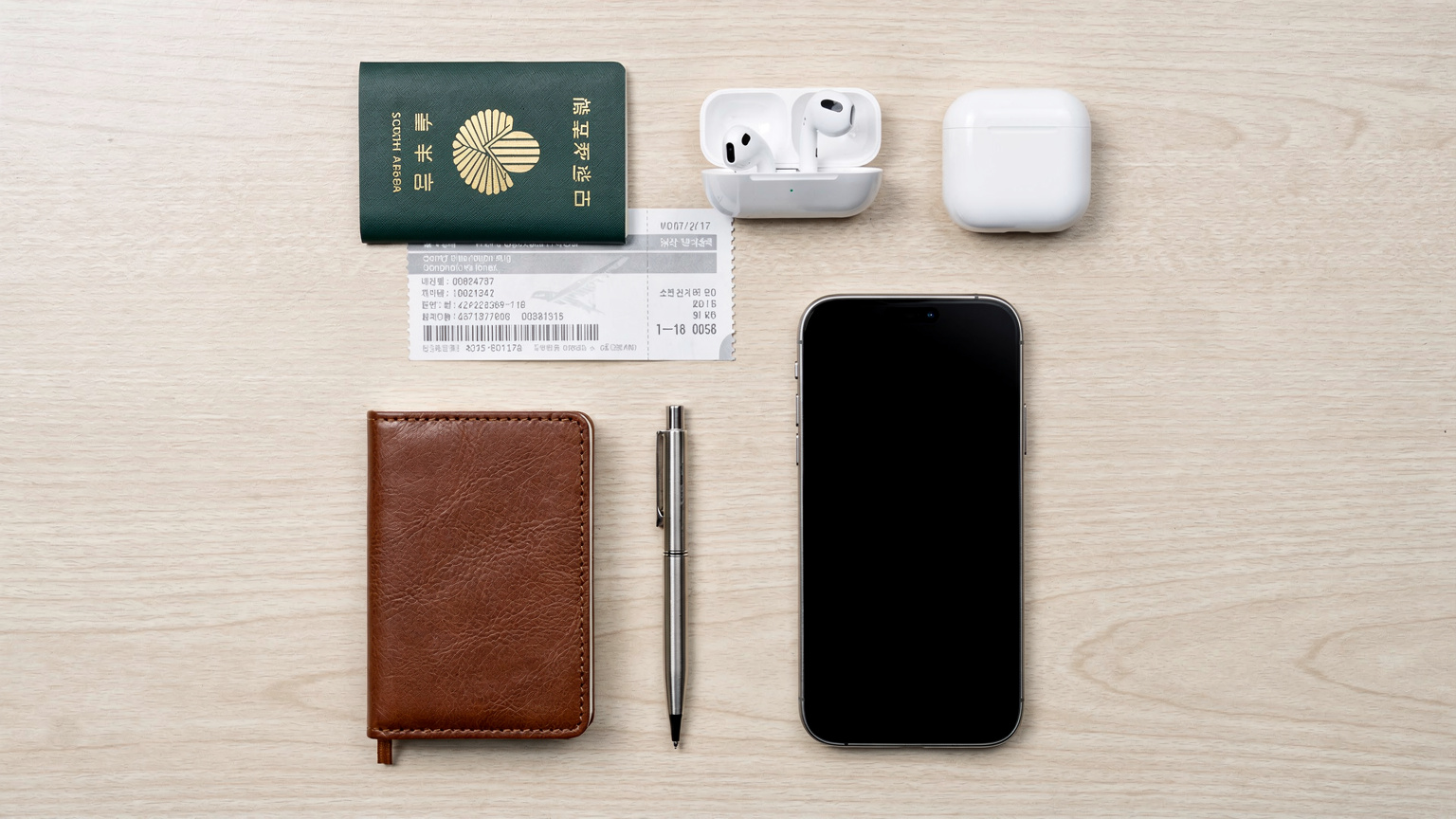 A neatly organized overhead flat-lay of travel essentials on a light wooden table, including an iPhone 17, a passport, a boarding pass, a small notebook, and a pen, signifying meticulous travel preparation.