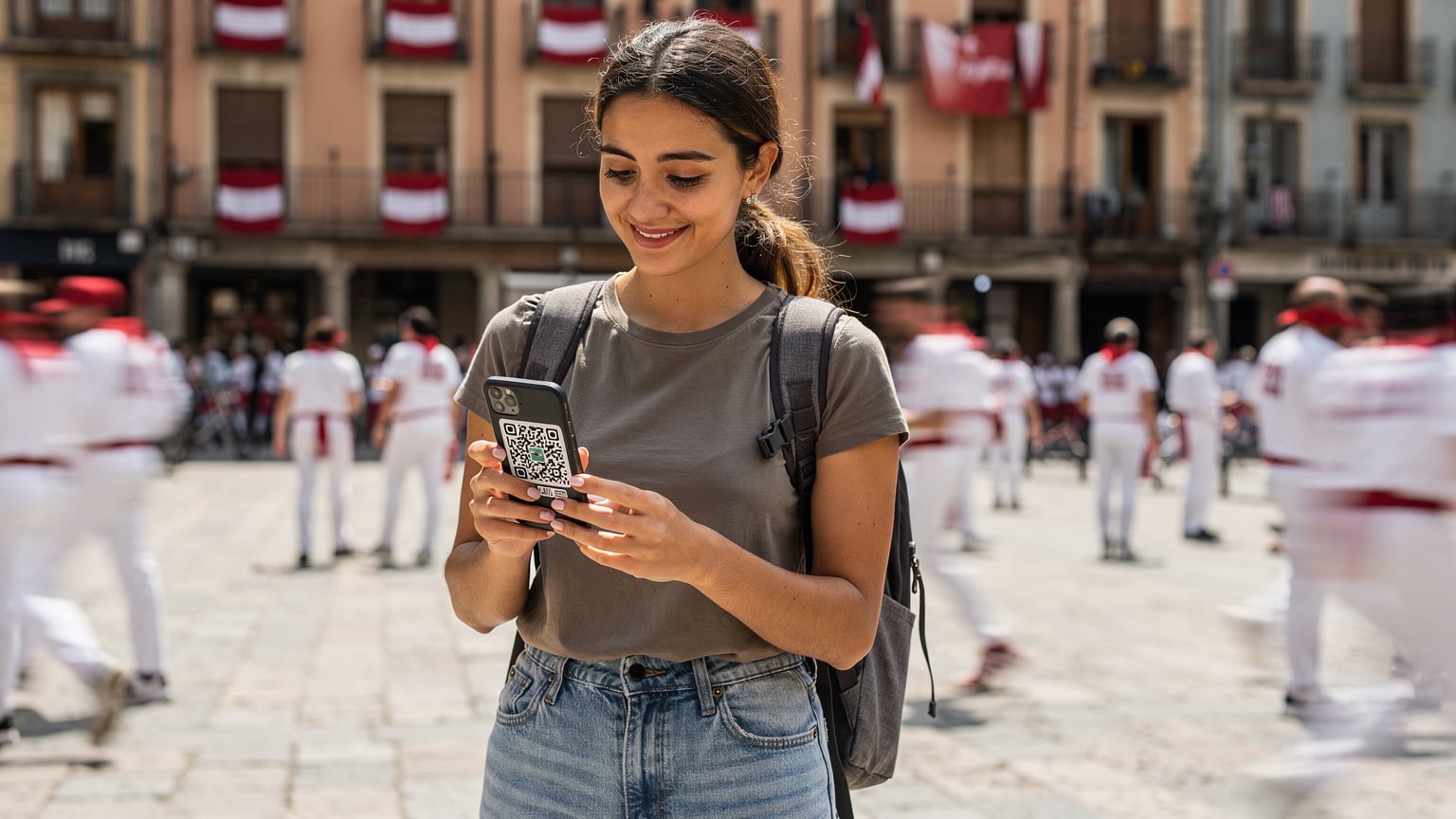 A digital nomad in a crowded Pamplona square, easily setting up her eSIM with a QR code on her phone, avoiding the hassle of finding a physical SIM card vendor.