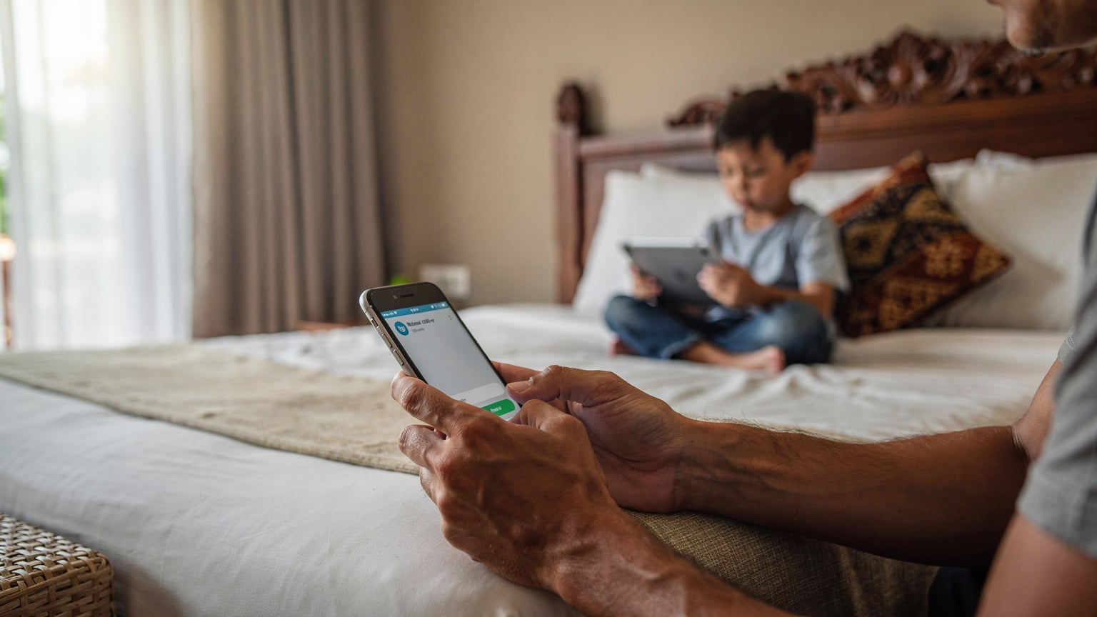 Un parent ajustant les paramètres de contrôle parental sur son smartphone, avec un enfant jouant sur une tablette en arrière-plan.