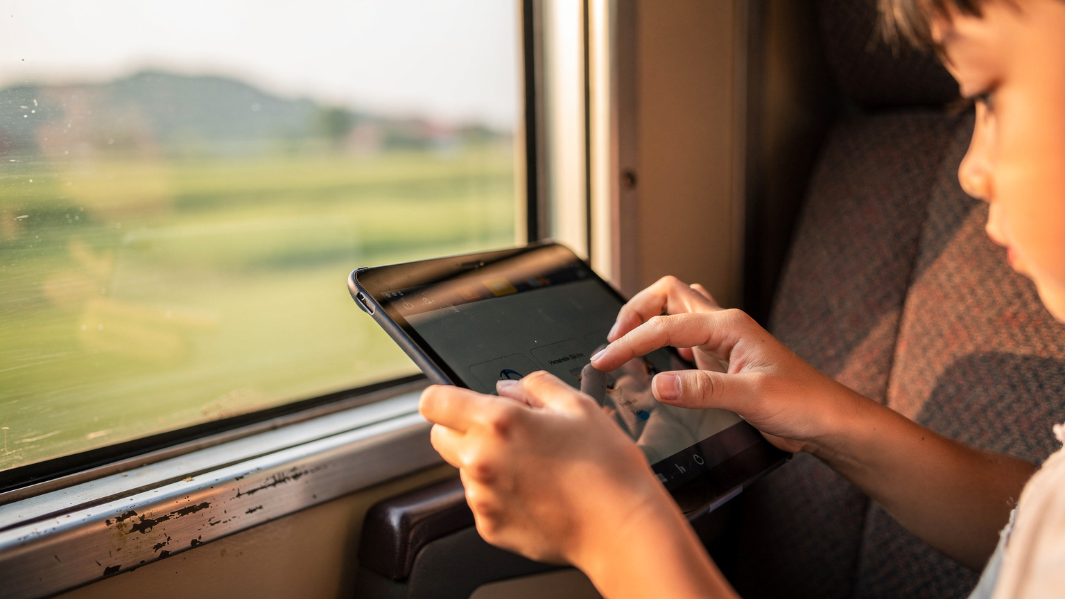 Gros plan sur des mains d'enfant tenant une tablette, illustrant le partage de connexion eSIM pour le divertissement en voyage.