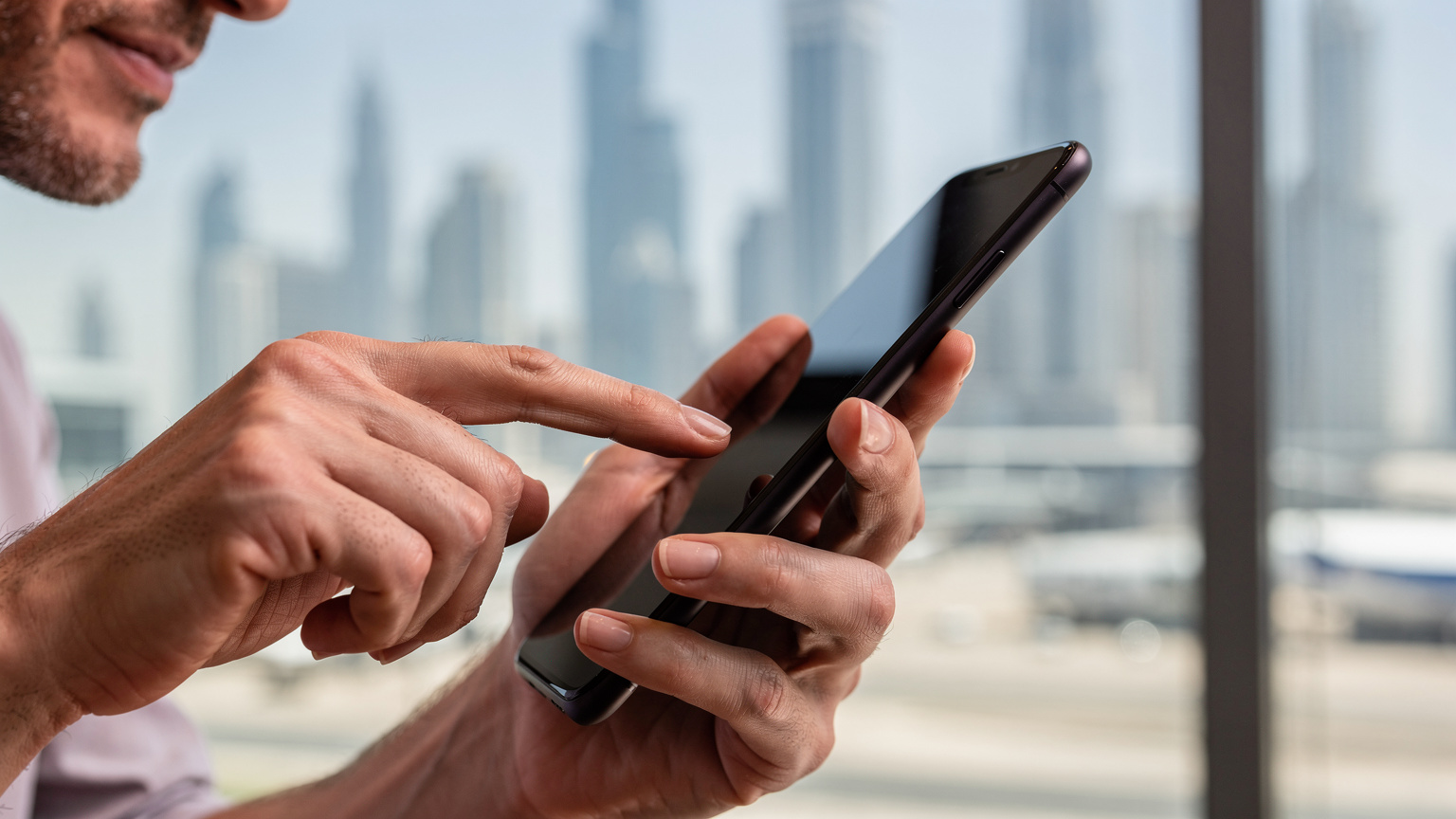 A close-up of a traveler's hands interacting with a smartphone, showing the ease of activating a global eSIM in an airport setting, with a blurred view of Dubai's skyline in the background.