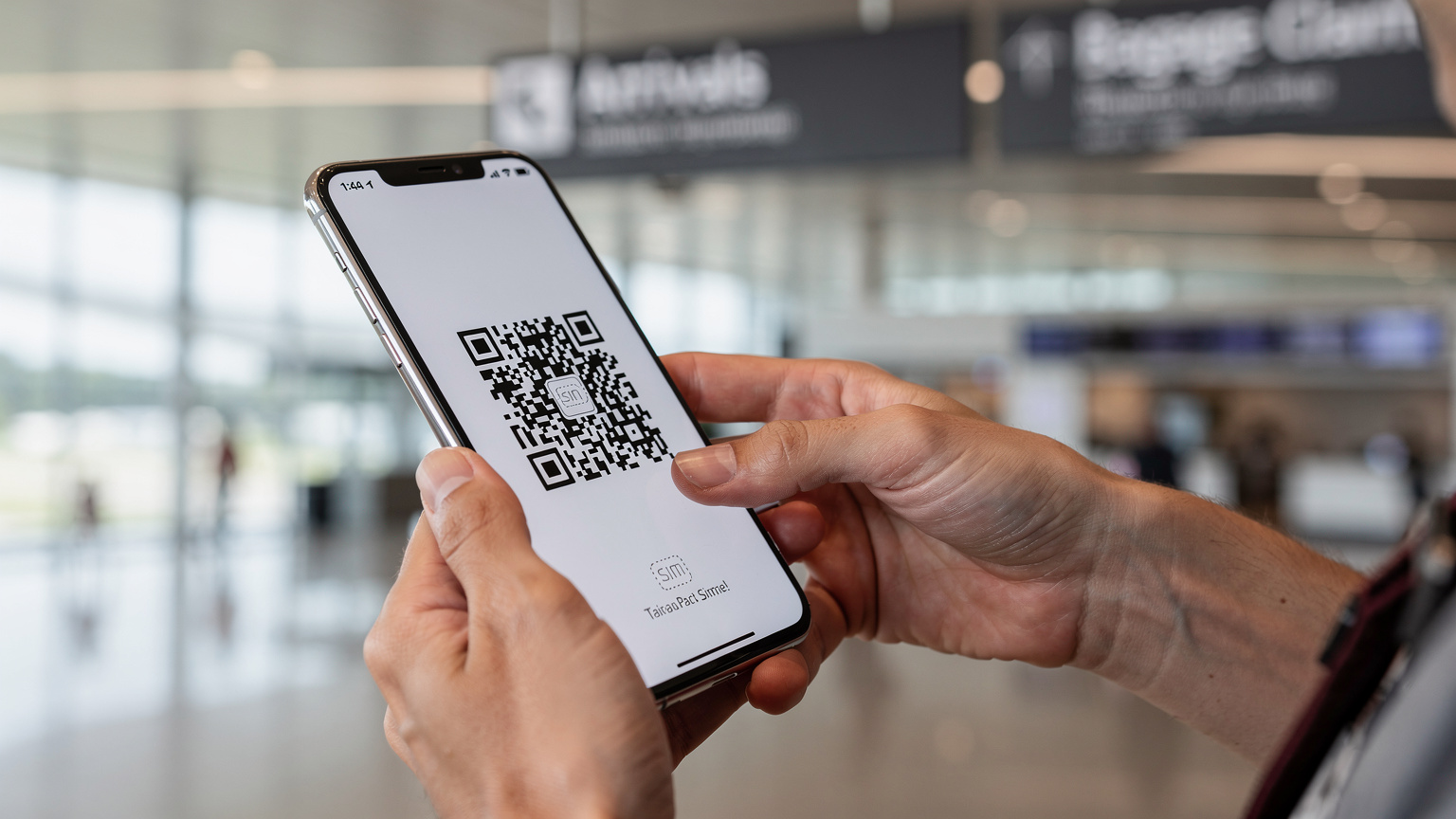 Nahaufnahme eines Smartphones in der Hand eines Reisenden, der gerade einen QR-Code für die eSIM-Installation scannt, mit einem verschwommenen Hintergrund der Ankunftshalle des Flughafens Chiang Mai.