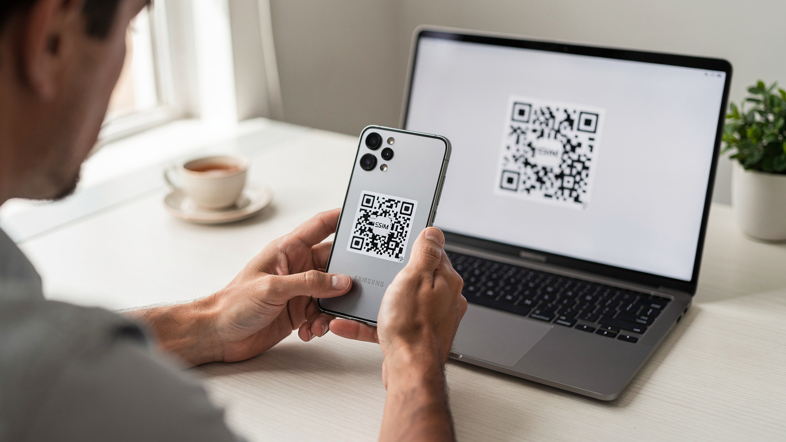 Deux mains tiennent un Samsung Galaxy S25, le positionnant pour scanner un QR code eSIM affiché sur un écran d'ordinateur portable, dans un environnement de bureau minimaliste.