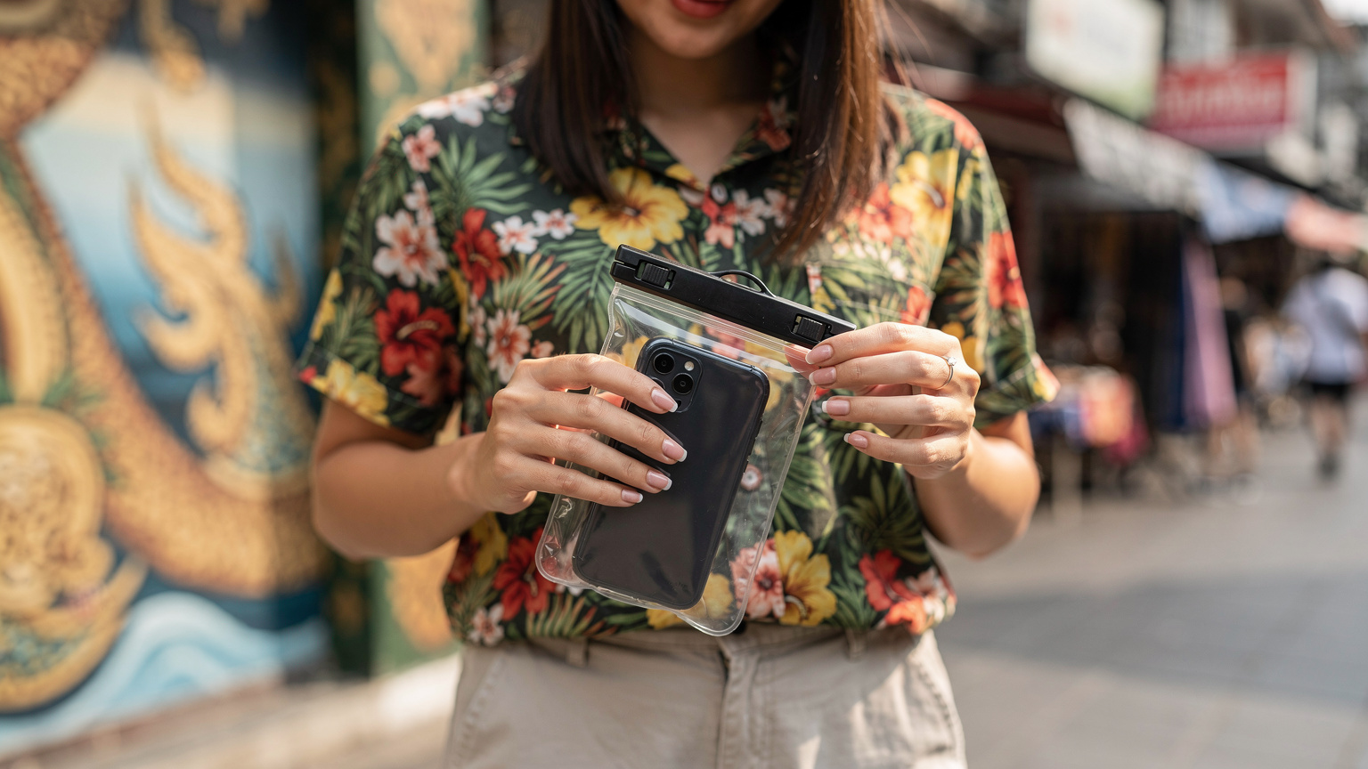 A traveler carefully sealing their smartphone in a waterproof pouch before joining the Songkran festivities in Bangkok, ensuring it's protected from water damage.