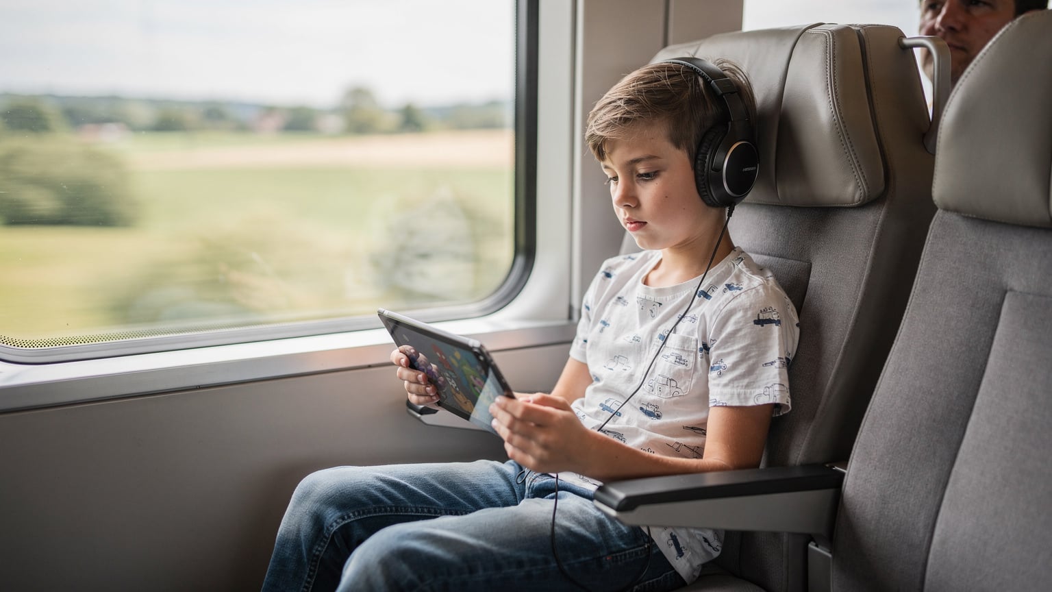 A child engrossed in a tablet, streaming a cartoon, while sitting comfortably on a train seat, illustrating how eSIM provides seamless entertainment during travel.