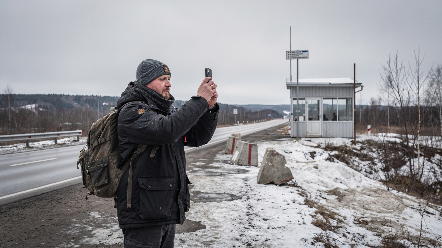 Турист стоит у пограничного столба на российско-финской границе, проверяя свой телефон, чтобы убедиться в наличии мобильной связи.