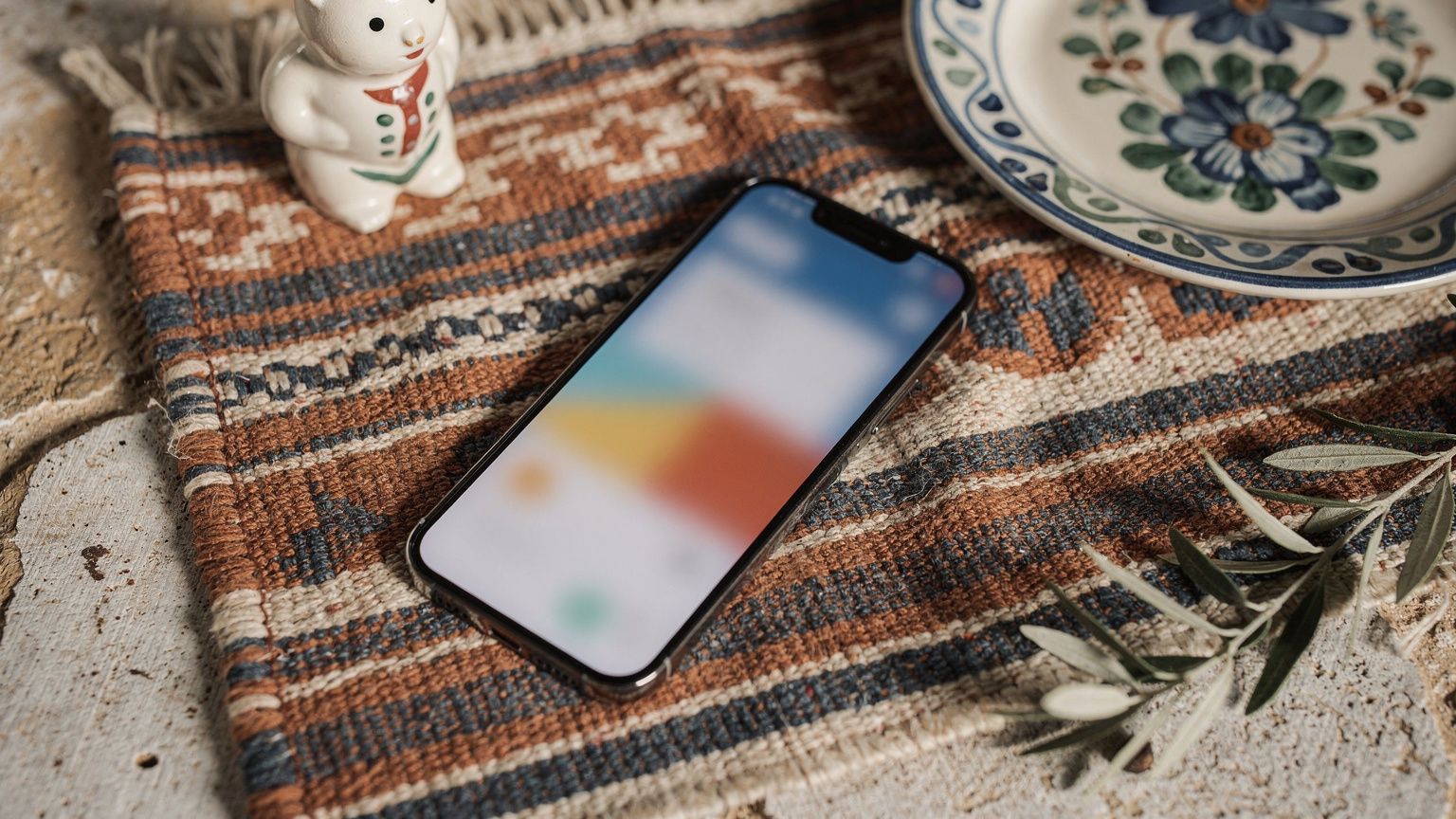 Eine Nahaufnahme zeigt ein Smartphone auf einer bunten mallorquinischen Decke. Auf dem Bildschirm ist eine Webseite mit verschiedenen eSIM-Tarifoptionen für Spanien geöffnet. Im Hintergrund sind unscharf traditionelle Keramik und ein Olivenzweig zu sehen.
