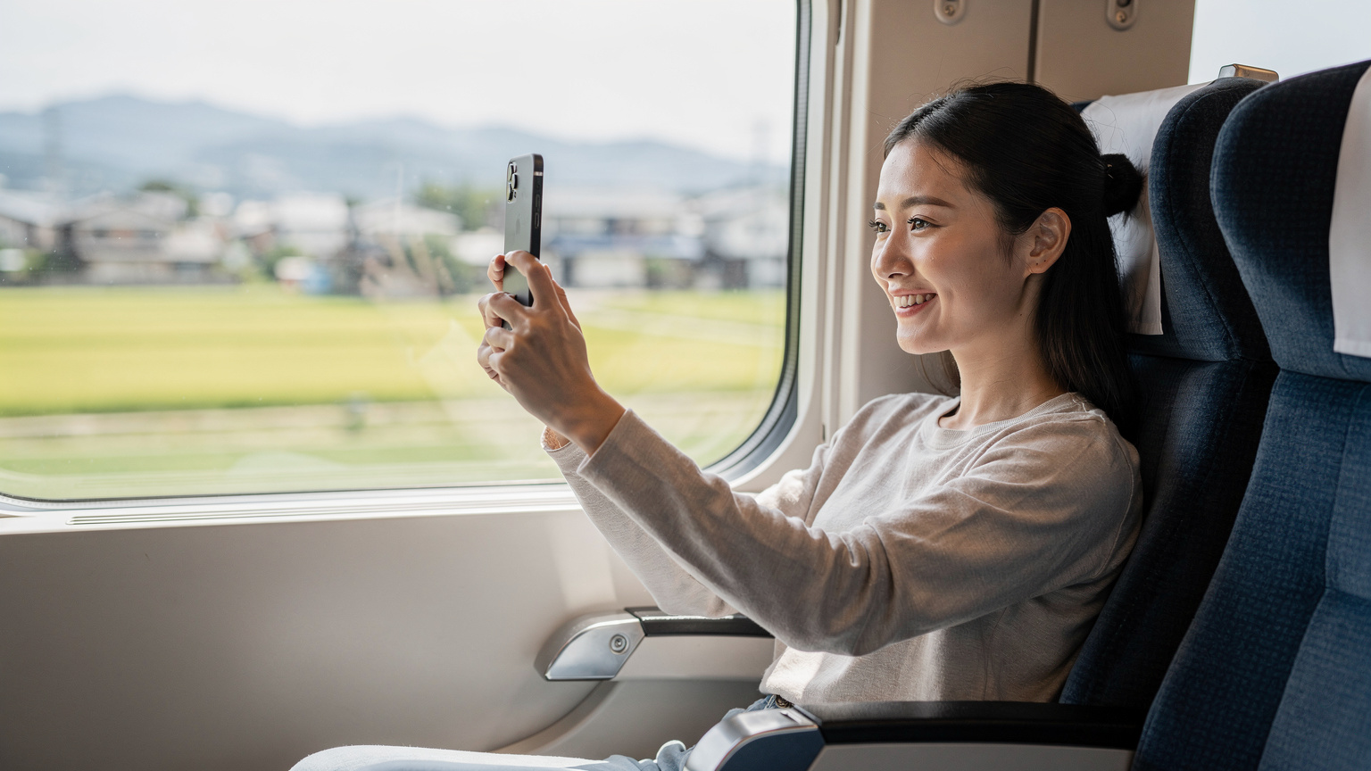 一位旅客在日本新干线列车上，正通过手机eSIM连接网络进行视频通话，窗外是飞驰而过的日本乡村景色。