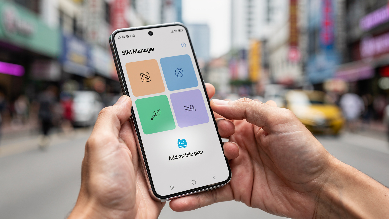 Tangan seorang pengembara memegang Samsung Galaxy S25 dengan tetingkap tetapan 'Pengurus SIM' terbuka, menunjuk ke pilihan 'Tambah pelan mudah alih'. Latar belakang kabur menunjukkan pemandangan jalan bandar.
