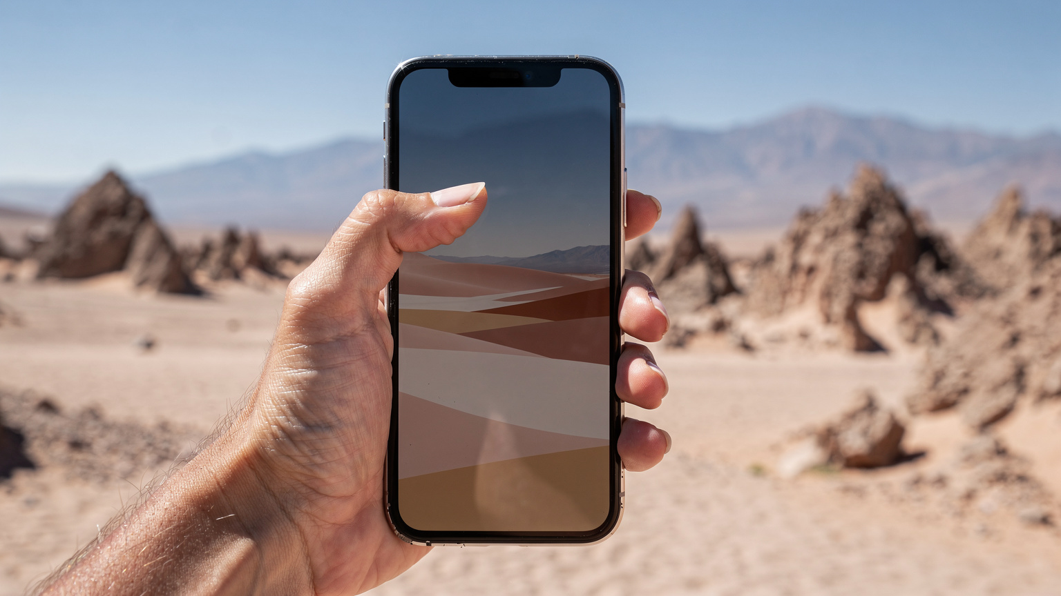 Uma mão feminina segura um smartphone mostrando um mapa offline, enquanto o polegar navega pela tela, em um cenário árido e vasto do Deserto do Atacama com formações rochosas e montanhas distantes.