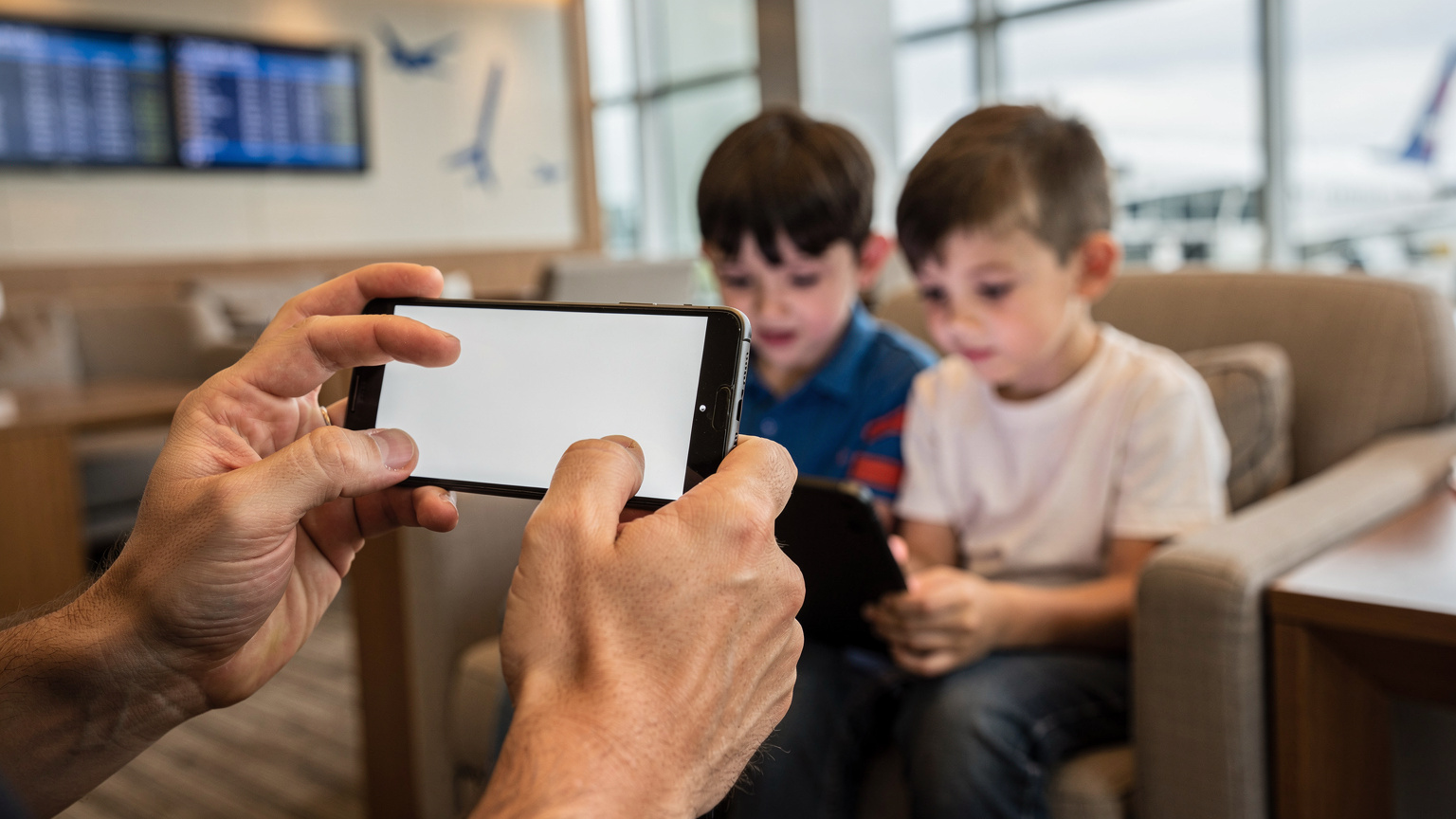 Un parent aide ses deux enfants à partager la connexion internet de son smartphone vers une tablette pour regarder un dessin animé, à l'intérieur d'un salon d'aéroport climatisé à Bangkok.