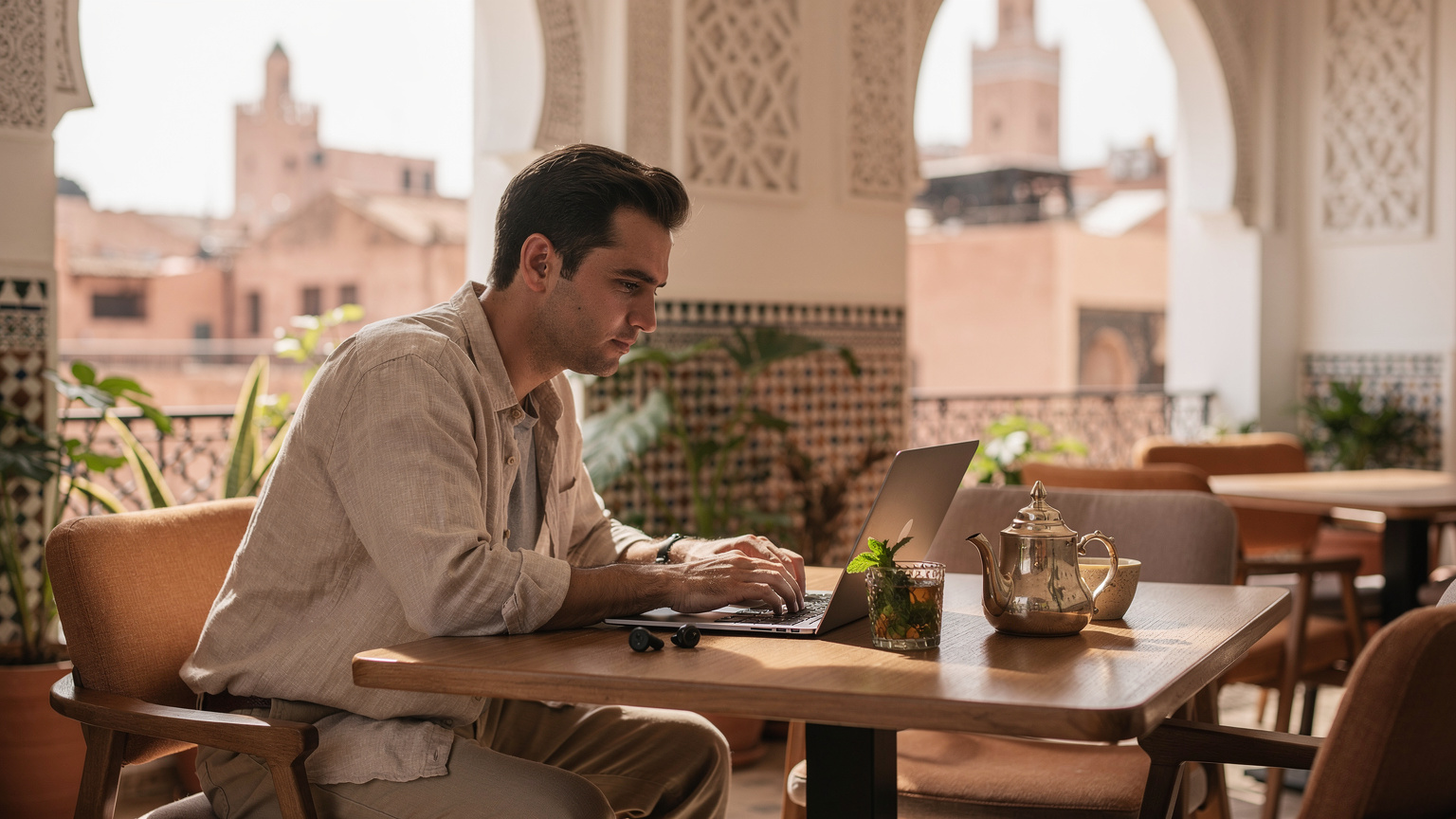 Ein Digital-Nomade arbeitet konzentriert an seinem Laptop in einem Co-Working-Space in Marrakesch, mit einer Tasse Minztee und marokkanischer Architektur im Hintergrund, was die nahtlose Integration von Arbeit und Reisen symbolisiert.