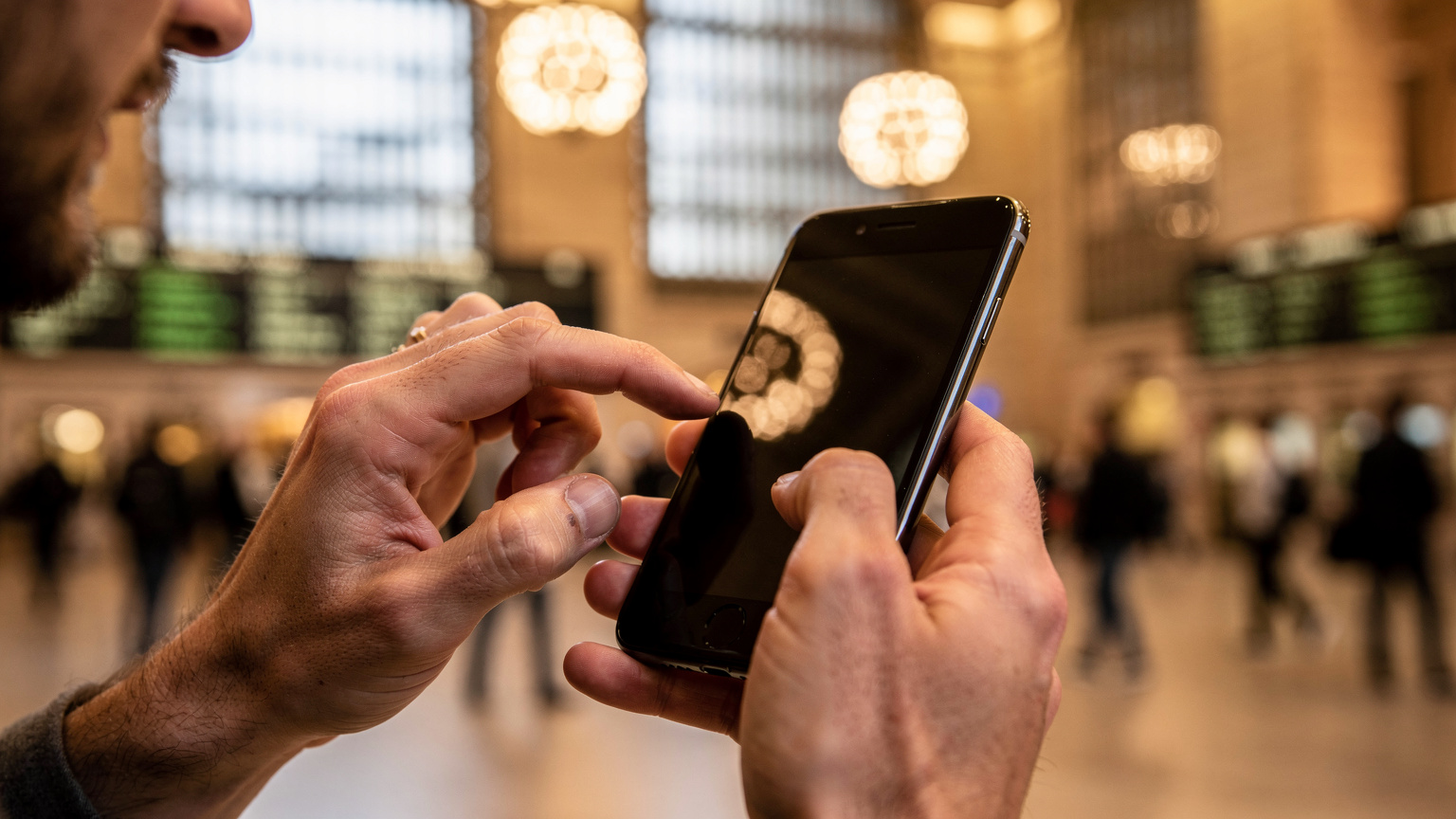 Detailní záběr na ruce cestovatele držícího telefon s aplikací eSIM, s rozmazaným pozadím rušného vlakového nádraží Grand Central Terminal.
