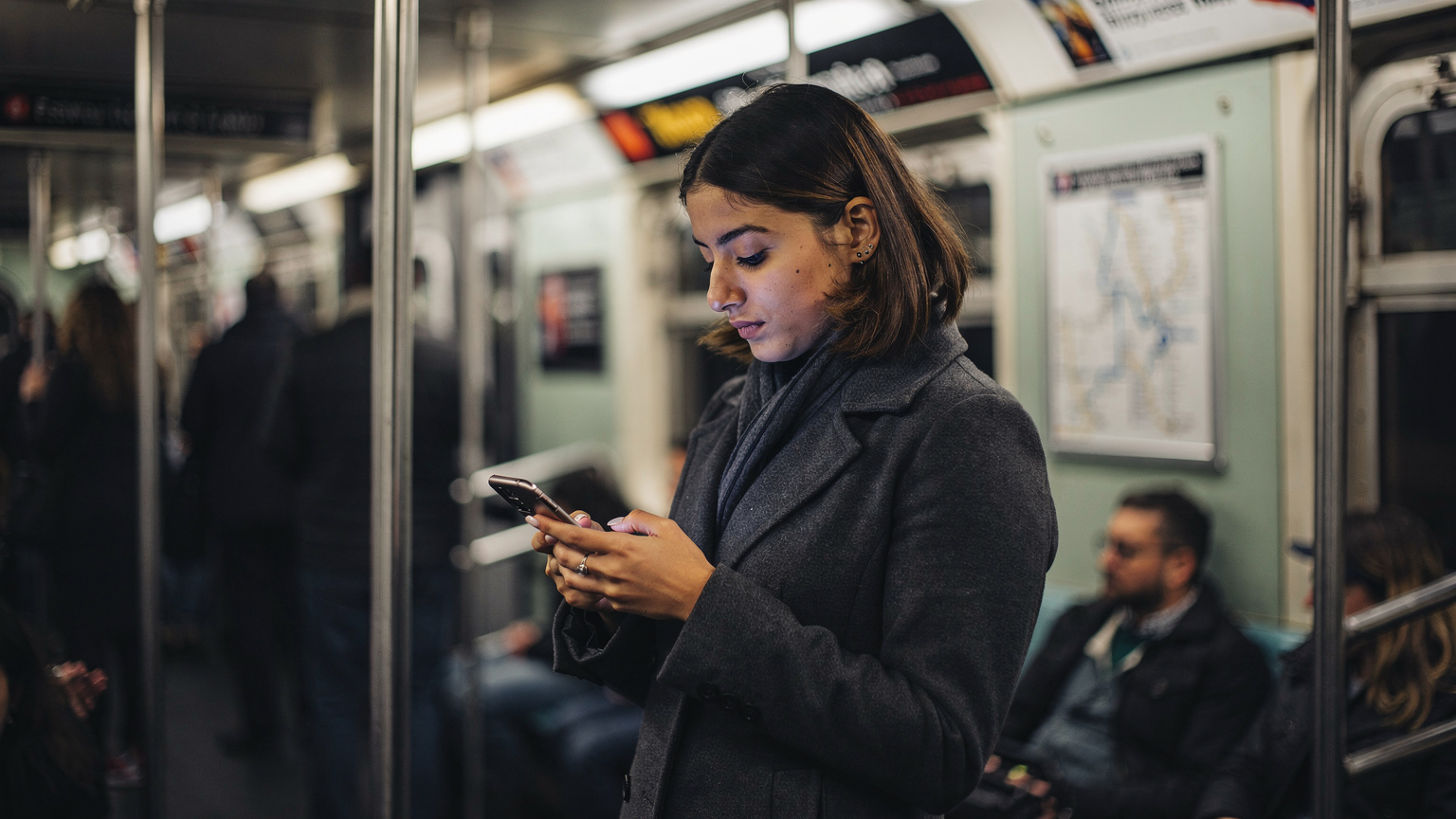 New York City metrosunda, kalabalık bir vagonda ayakta duran genç bir kadın, akıllı telefonunun ekranına dikkatlice bakıyor. eSIM bağlantısı sayesinde metrodayken bile haritalardan yol tarifi alabiliyor veya sosyal medyasını kontrol edebiliyor.