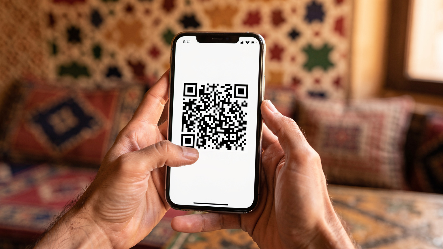 Крупeн план на ръце, държащи смартфон, показващ QR код за активиране на eSIM, на фона на традиционен египетски декор.