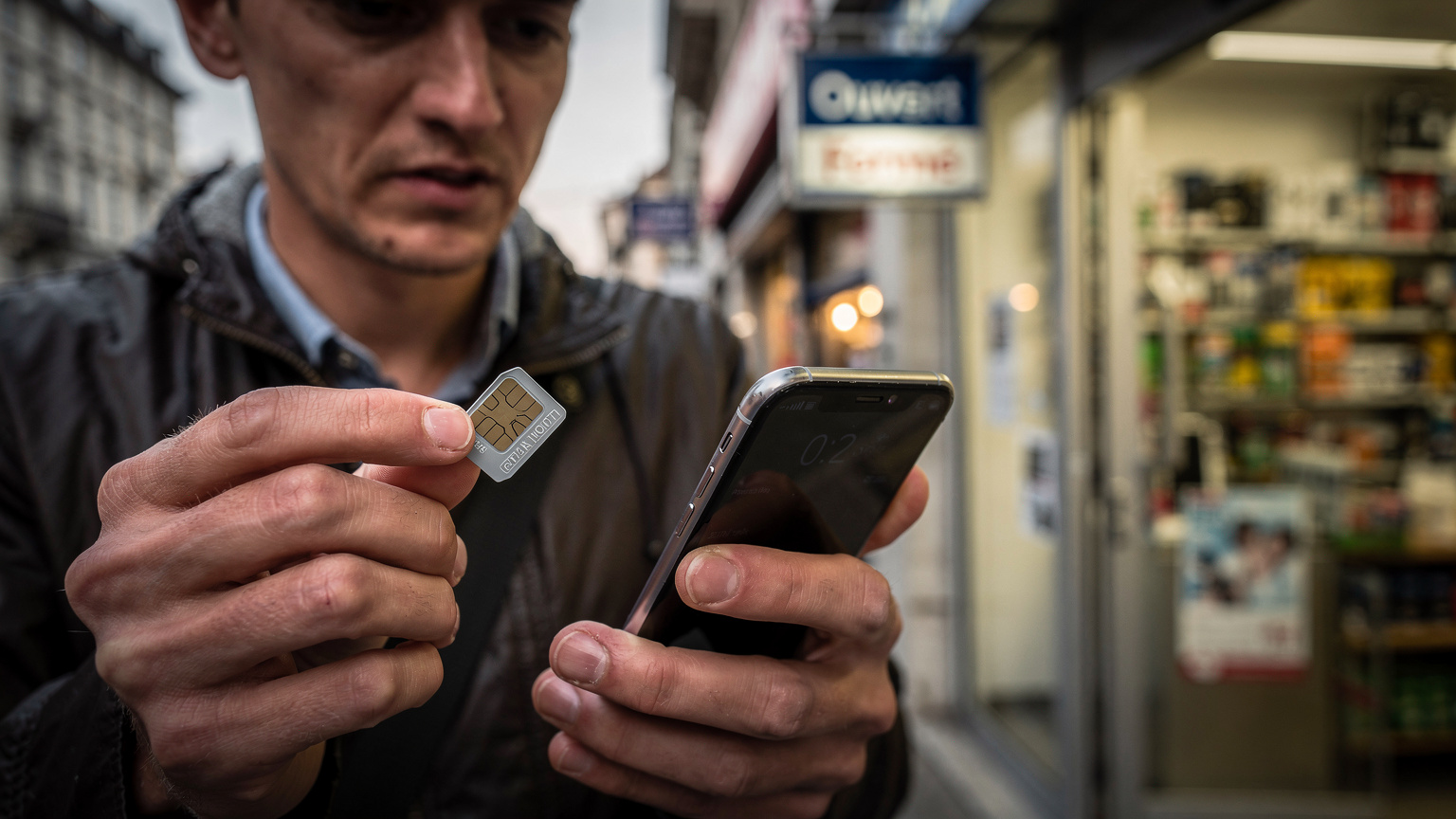 Eine Person hält an einem Kiosk in Genf eine lokale physische SIM-Karte und ihr Smartphone, während sie die Uhrzeit prüft, um festzustellen, ob der Laden noch geöffnet ist.