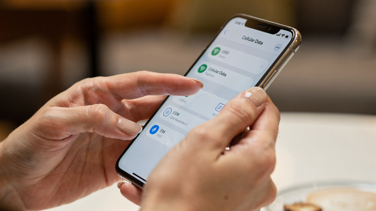 Tangan seorang wanita memegang telefon pintar yang memaparkan tetapan rangkaian, dengan jari menunjuk ke pilihan 'Data Selular' atau 'eSIM', menunjukkan interaksi pengguna.