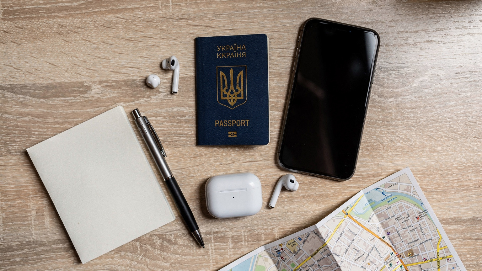 Охайно організований робочий стіл мандрівника з паспортом, смартфоном, навушниками та картою.