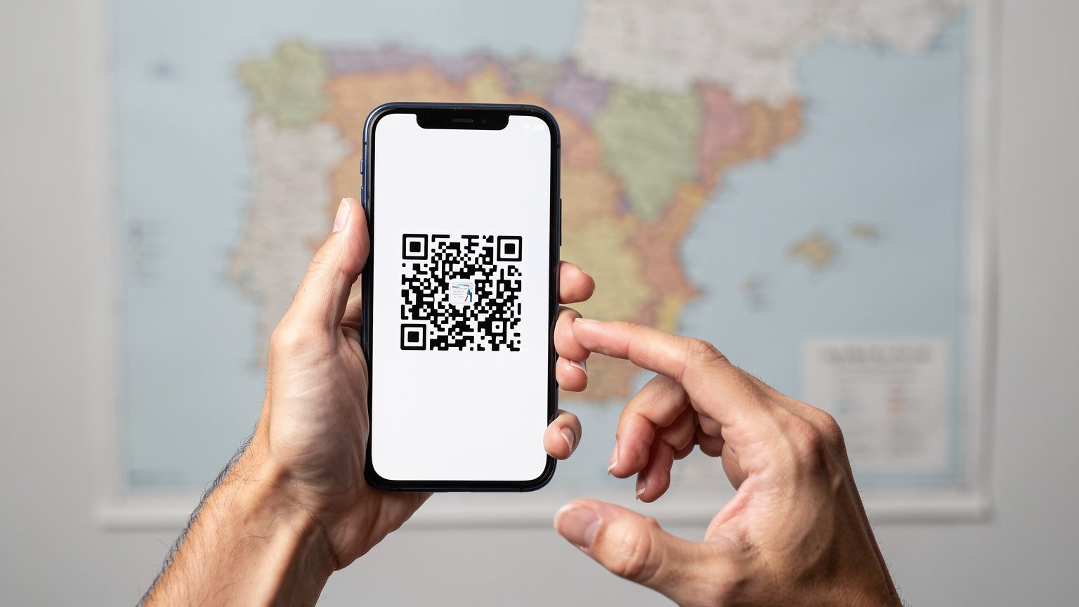Ręce trzymające smartfon, na którym wyświetlony jest kod QR do aktywacji eSIM, w tle rozmazana mapa Hiszpanii.