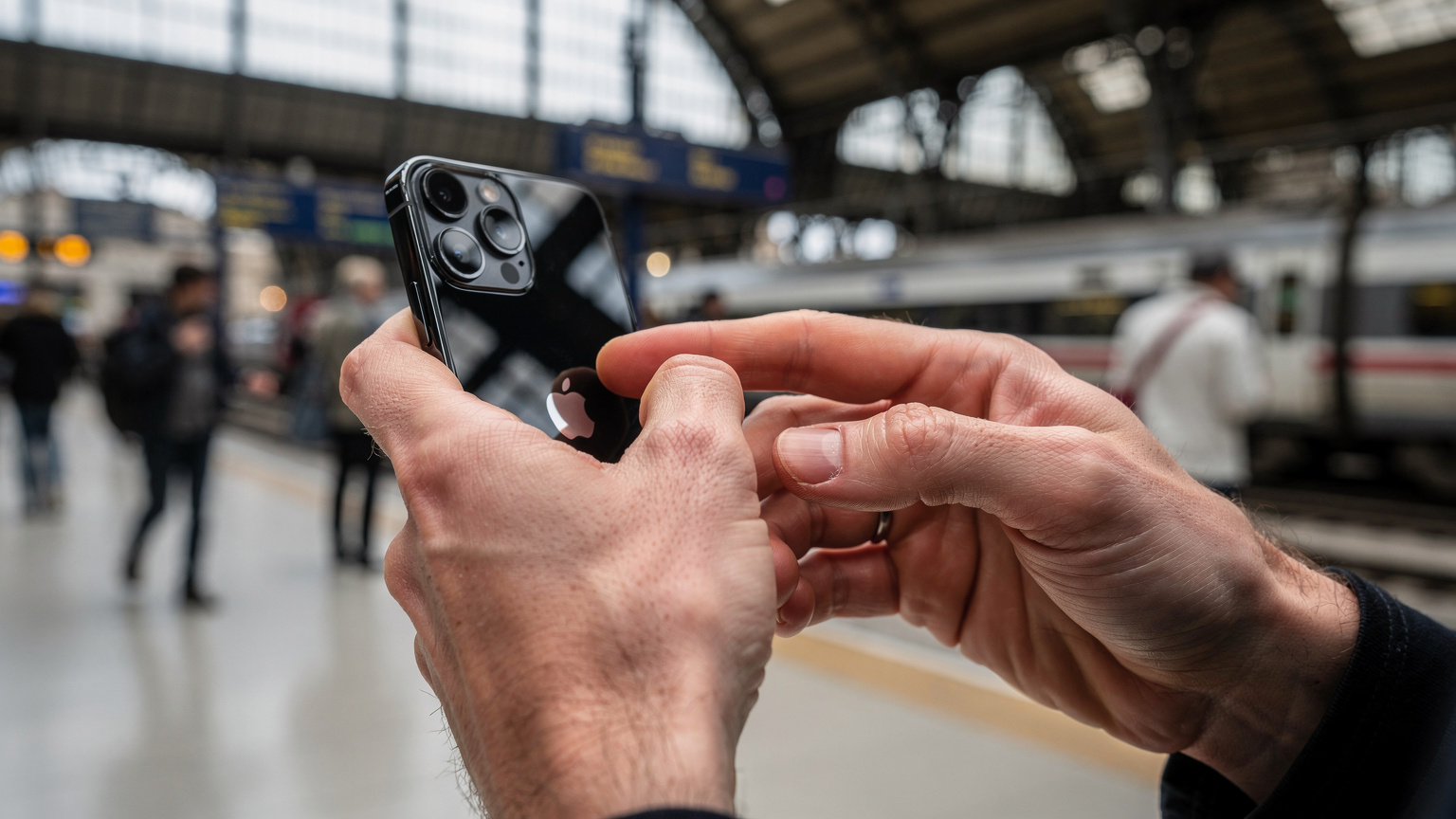 A close-up of a parent's hands, looking concerned, interacting with an iPhone 15 in a busy European train station, trying to troubleshoot a connectivity issue.