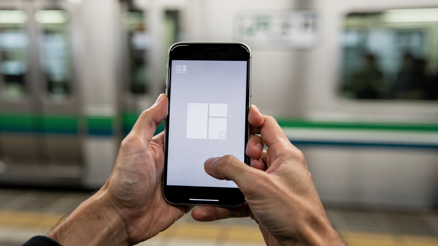 A close-up of a traveler's hands holding a smartphone displaying an eSIM activation screen, set against the blurred background of a Japanese train station platform, possibly the JR Yamanote line.