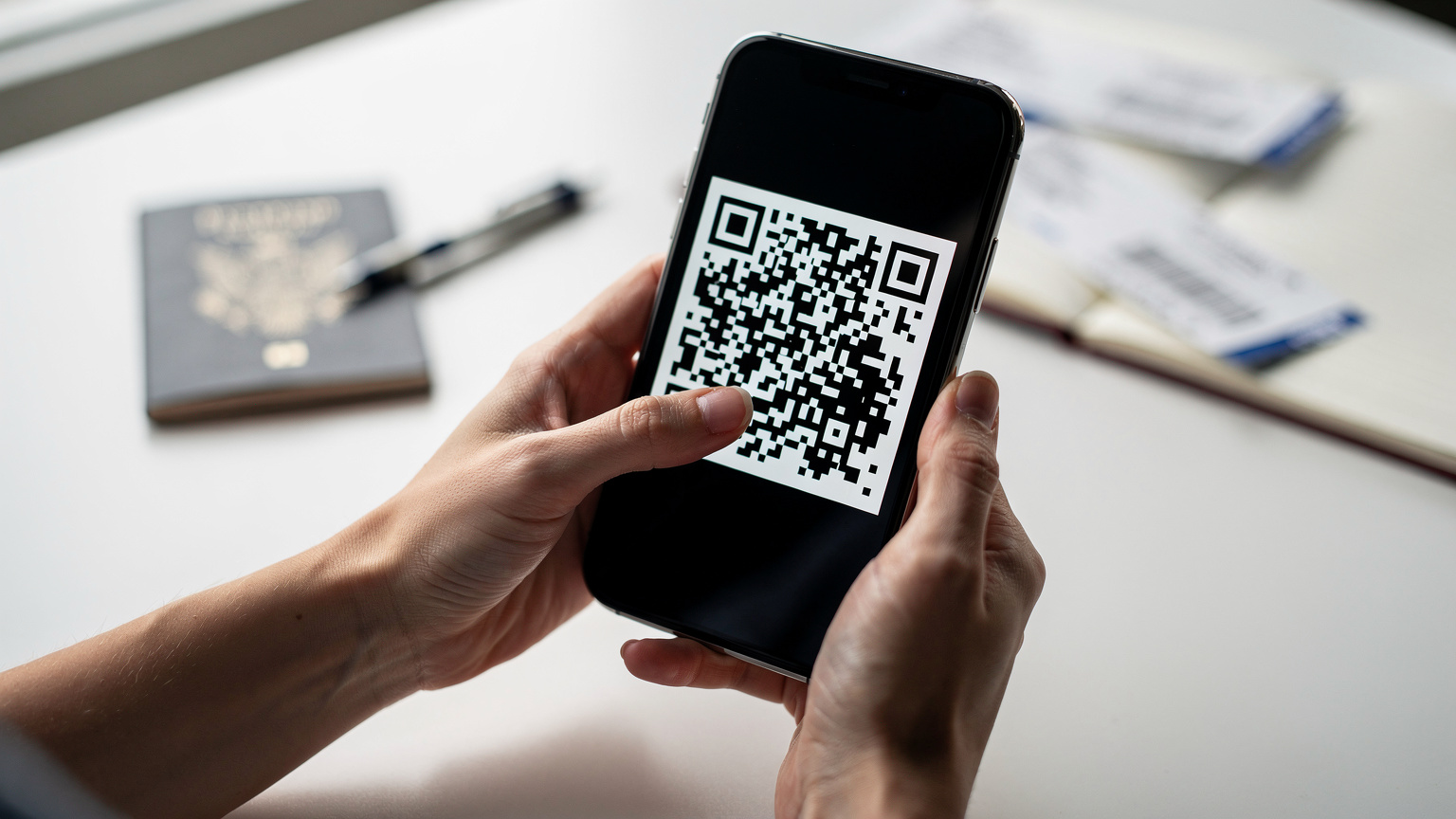 Nahaufnahme von Händen, die ein Smartphone halten und einen QR-Code scannen, um eine eSIM zu aktivieren. Die Finger zeigen auf den Bildschirm, der den QR-Code anzeigt. Der Hintergrund ist leicht unscharf und zeigt eine Reisevorbereitungsszene mit Reisepass und Notizen.