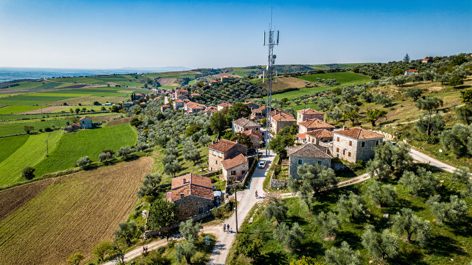 En drone-vy över den albanska landsbygden med traditionella hus och frodig grönska, med en modern mobilmast i fjärran, symboliserar täckning överallt.