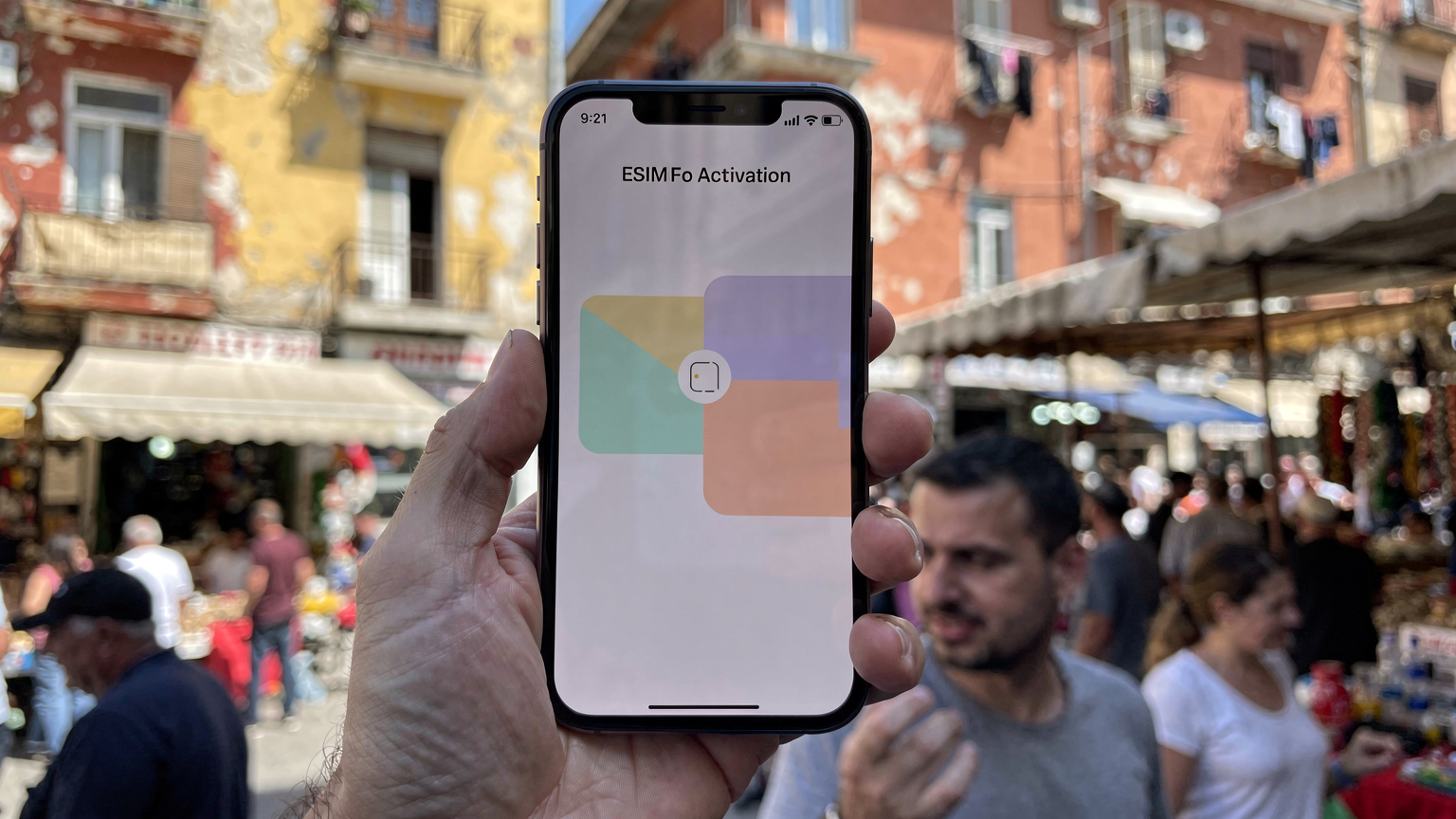 En mobiltelefon med ett eSIM-gränssnitt visas, med Tiranas pulserande stadsliv i bakgrunden, vilket symboliserar enkel anslutning.