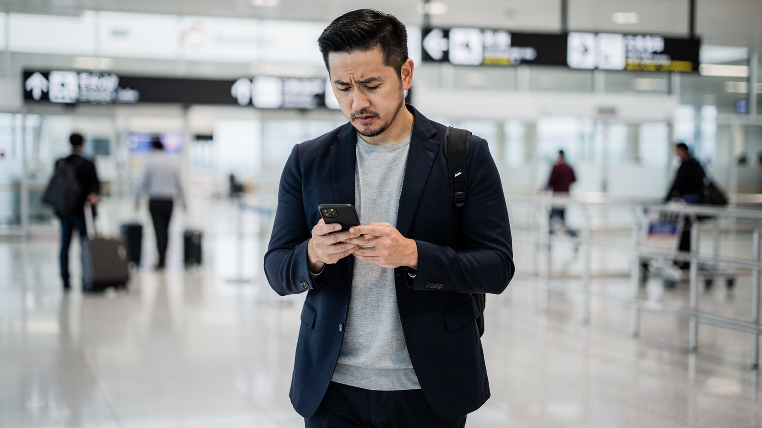 一位旅客在日本羽田機場的到達大廳，查看手機上的eSIM連接狀態，背景是熙熙攘攘的人群。