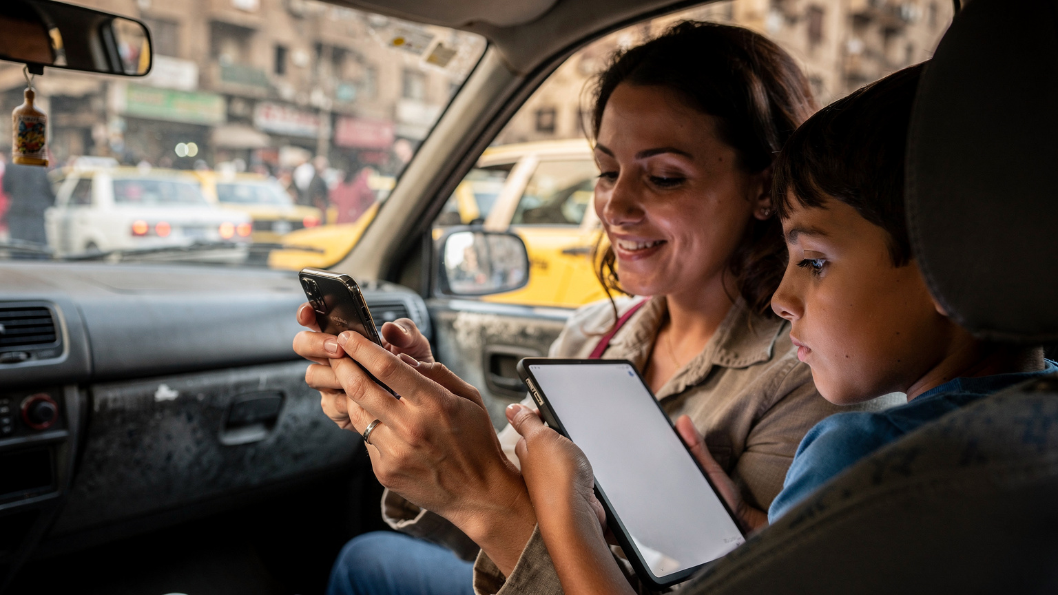 Una madre italiana mostra a suo figlio come connettersi all'hotspot del suo telefono, con un tablet in mano, all'interno di un taxi in attesa nel traffico de Il Cairo, Egitto.