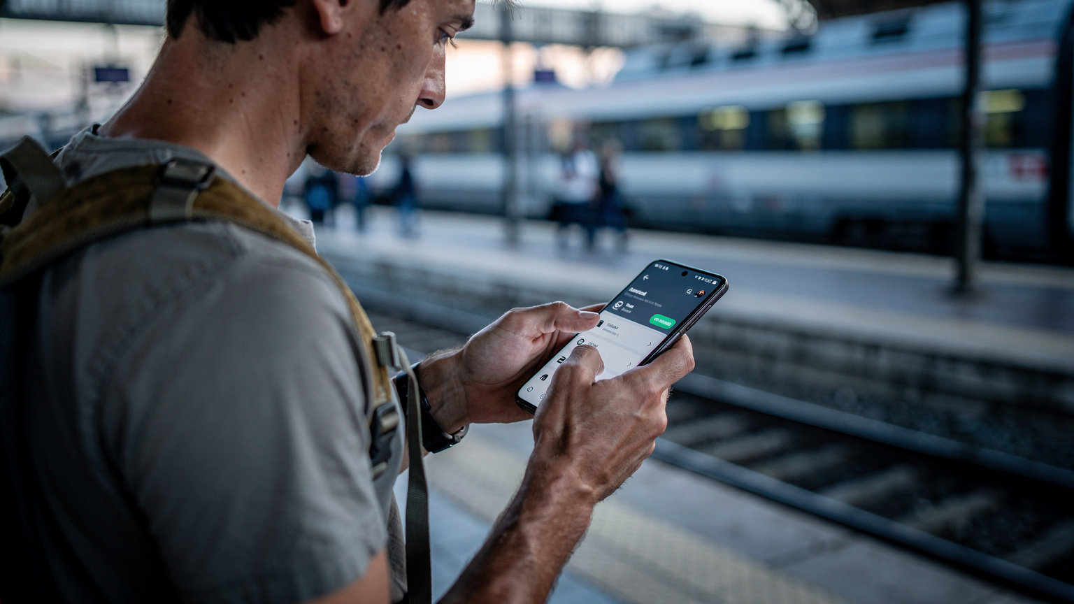 Un călător verifică cu atenție setările telefonului său Samsung Galaxy S26 pe peronul aglomerat al unei gări din Roma Termini, în lumina rece a dimineții, căutând opțiunea eSIM.