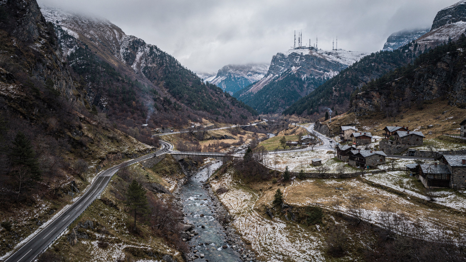 Vista aérea de la carretera principal que serpentea a través de un valle montañoso en Andorra, con pequeños pueblos y edificios dispersos a lo largo del camino, mostrando la infraestructura de telecomunicaciones en la distancia.