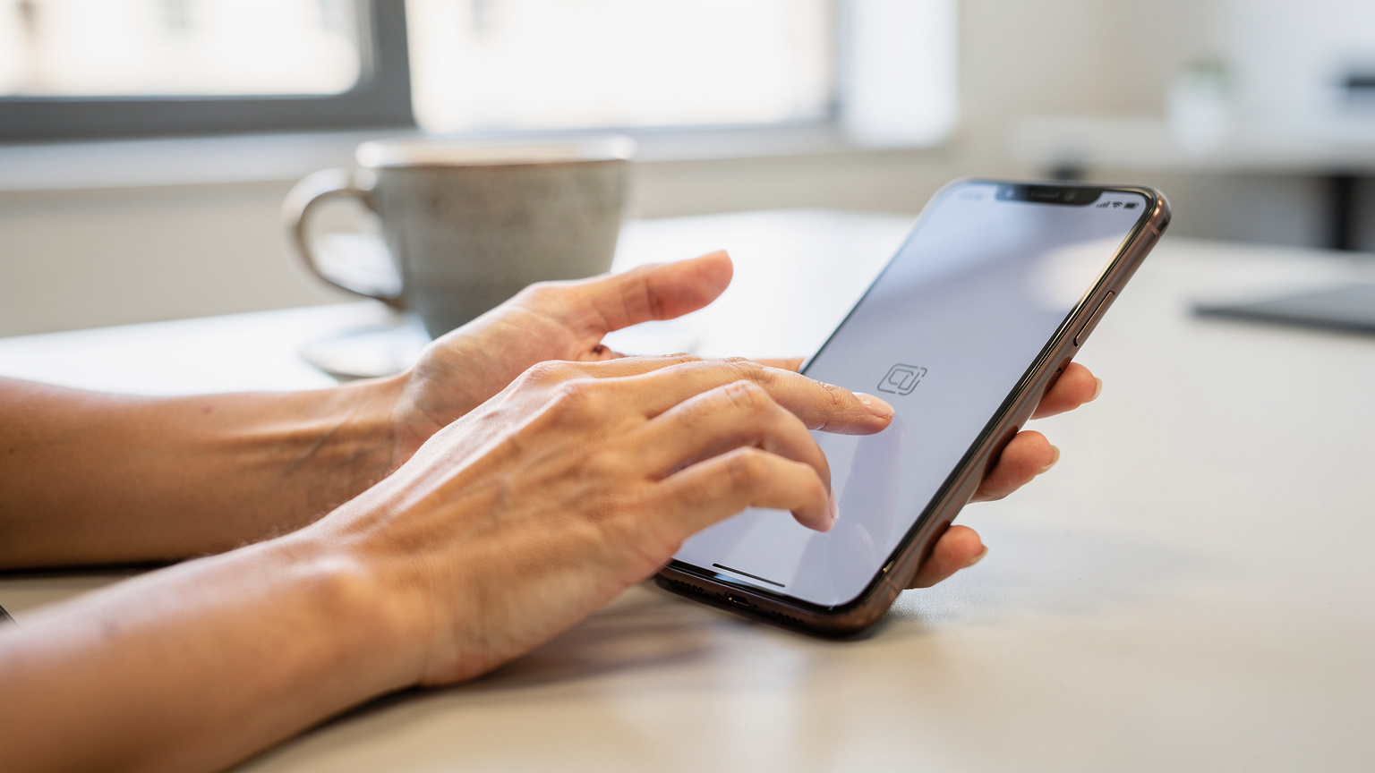 Mãos de uma mulher brasileira digitando em um smartphone, com foco na tela mostrando a interface de um aplicativo de eSIM, em um ambiente de coworking moderno em Lisboa, com um copo de café ao lado.