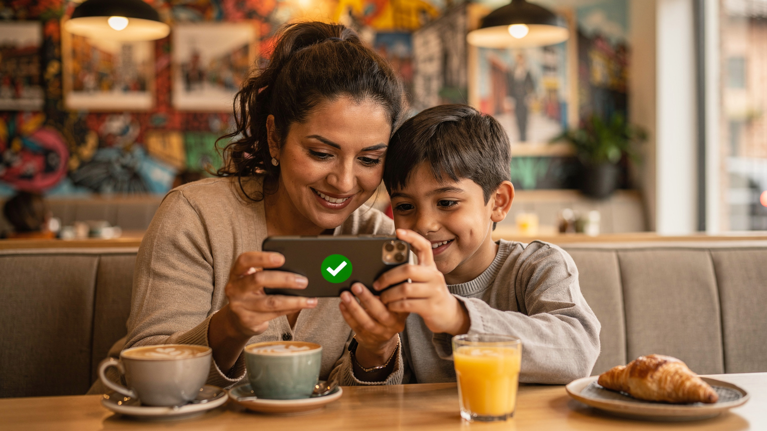 Une mère souriante et son enfant regardent ensemble l'écran d'un smartphone, montrant l'activation réussie d'une eSIM, dans un café confortable de La Floresta à Quito.