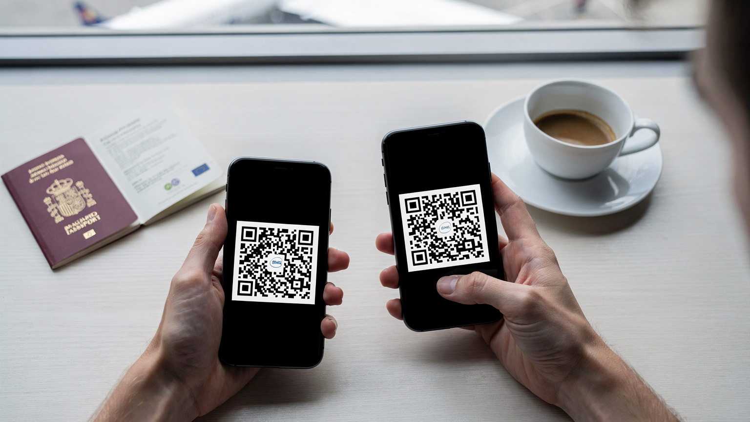 Manos de un viajero sosteniendo un smartphone, mostrando el proceso de escaneo de un código QR para activar una eSIM. Un pasaporte abierto de España y una taza de café están en la mesa de un aeropuerto de fondo, con la ventana de la terminal visible.