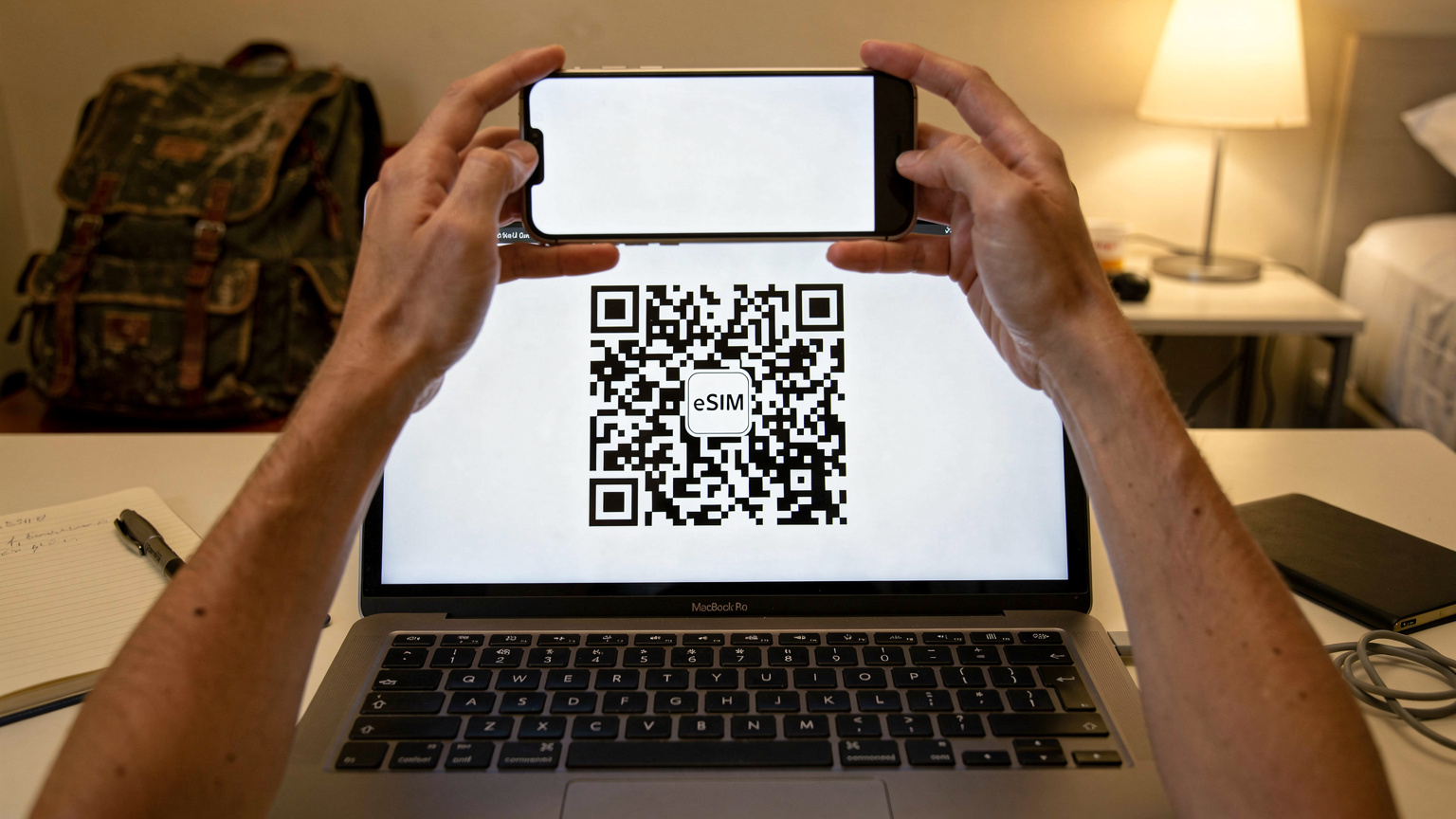 Close-up van een QR-code op een laptopscherm, met een smartphone die dichtbij wordt gehouden om de code te scannen. De scène speelt zich af in een nette, functionele hostelkamer in Willemstad, Curaçao, met een rugzak op de achtergrond.