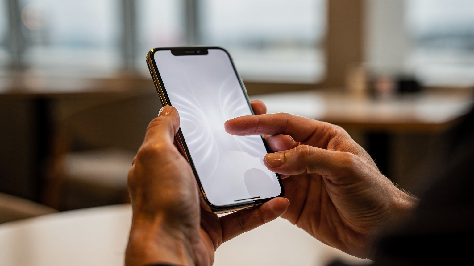 Close-up of a traveler's hands interacting with a smartphone, showing the tactile experience of navigating an eSIM app, with a blurred background of a cafe or airport lounge.